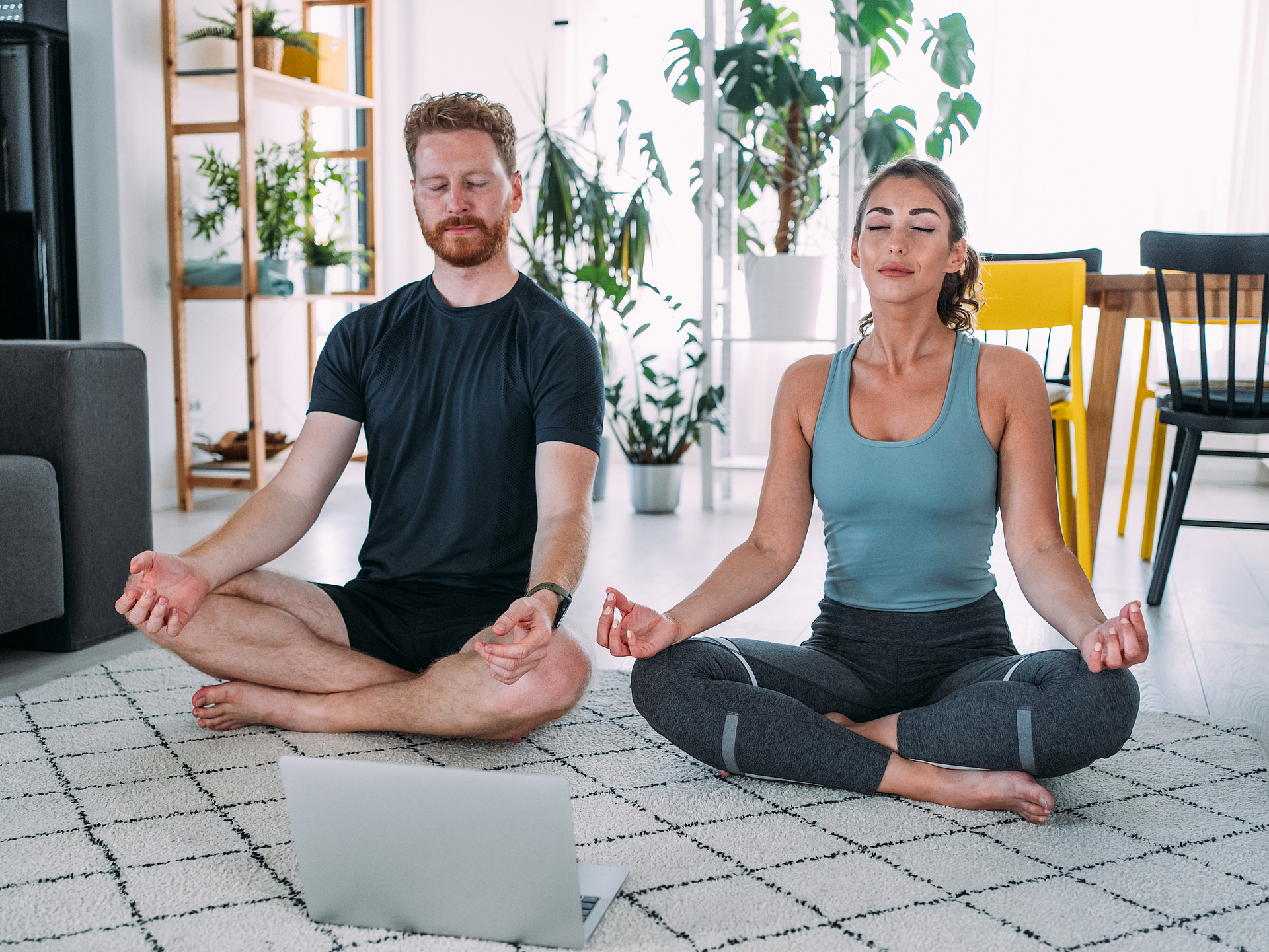 Mann und Frau im Schneidersitz machen Yoga im Wohnzimmer